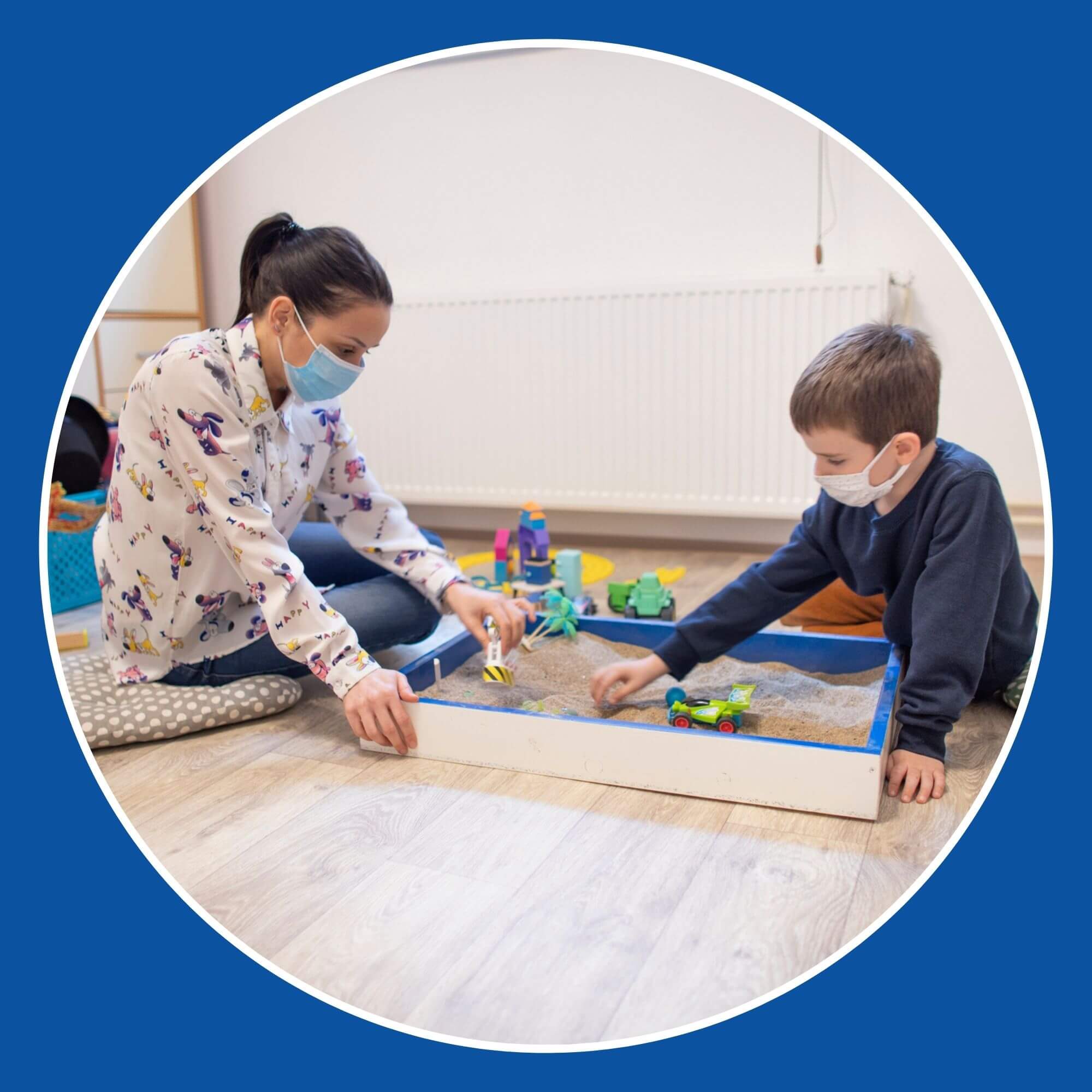 Image showing a young woman and young boy playing with toys in a sand play area. Image from iStock-13104219