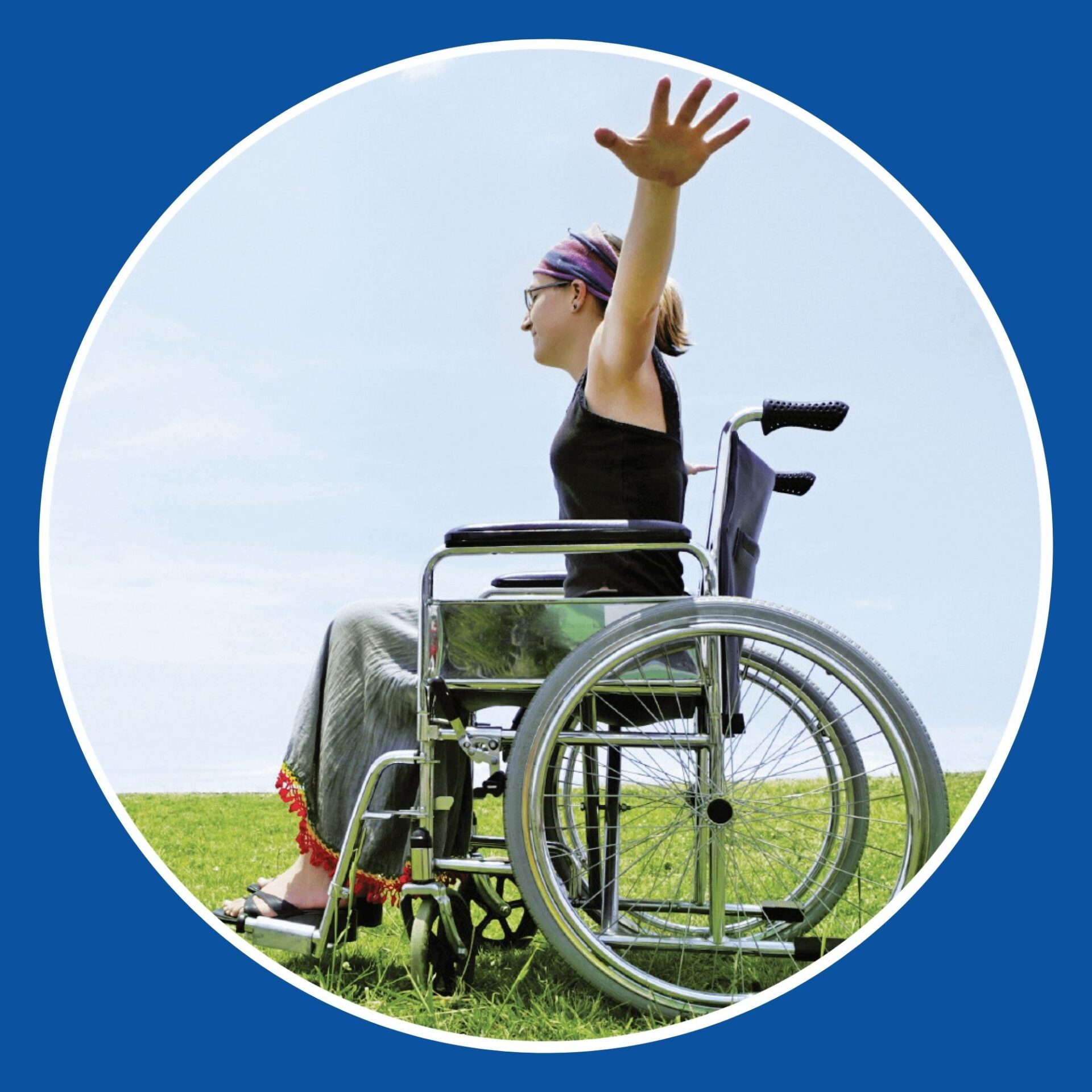 Image of a happy young lady with her arms in the air, in her wheelchair, on lush green grass
