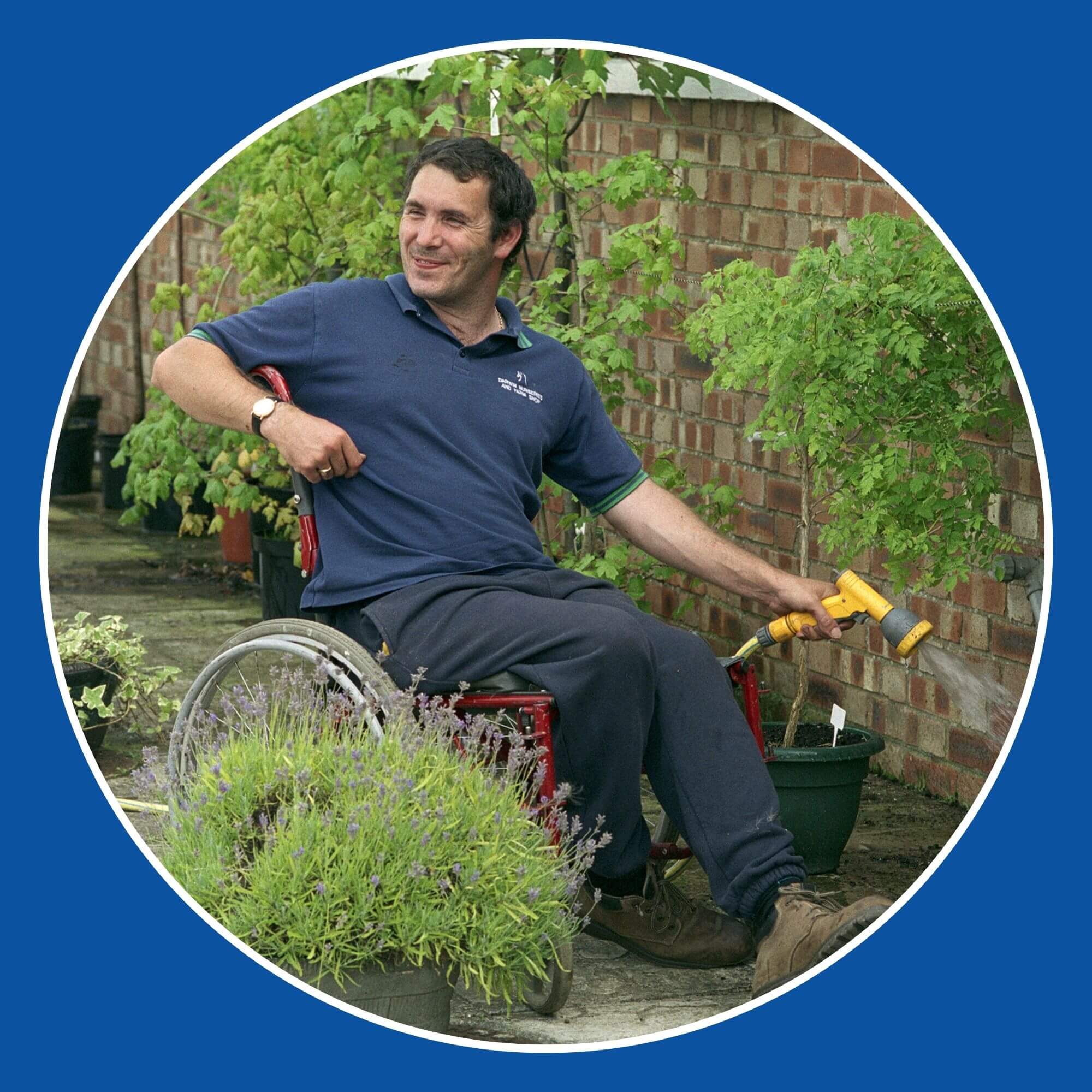 The photo shows a man in a wheelchair in his garden watering the plants