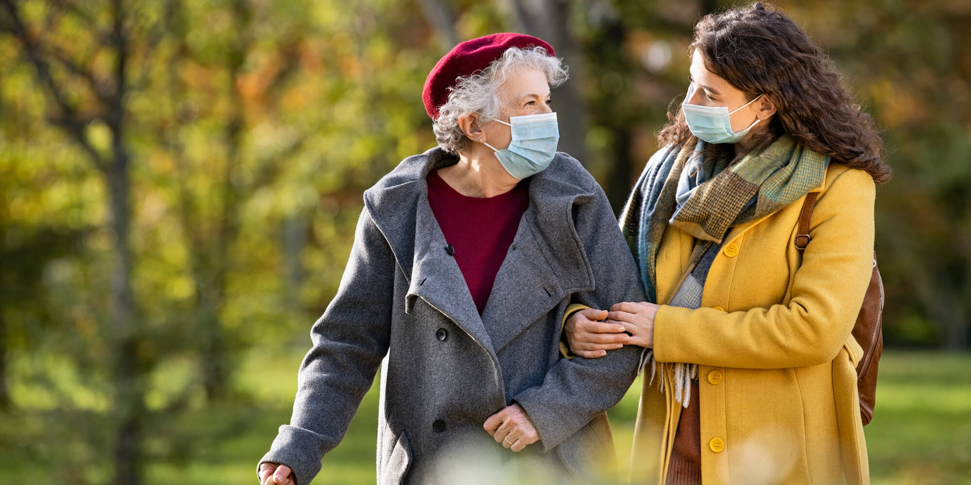 Photo showing an elderly lady walking through the park helped by a younger lady. Photo from iStock-1284869697