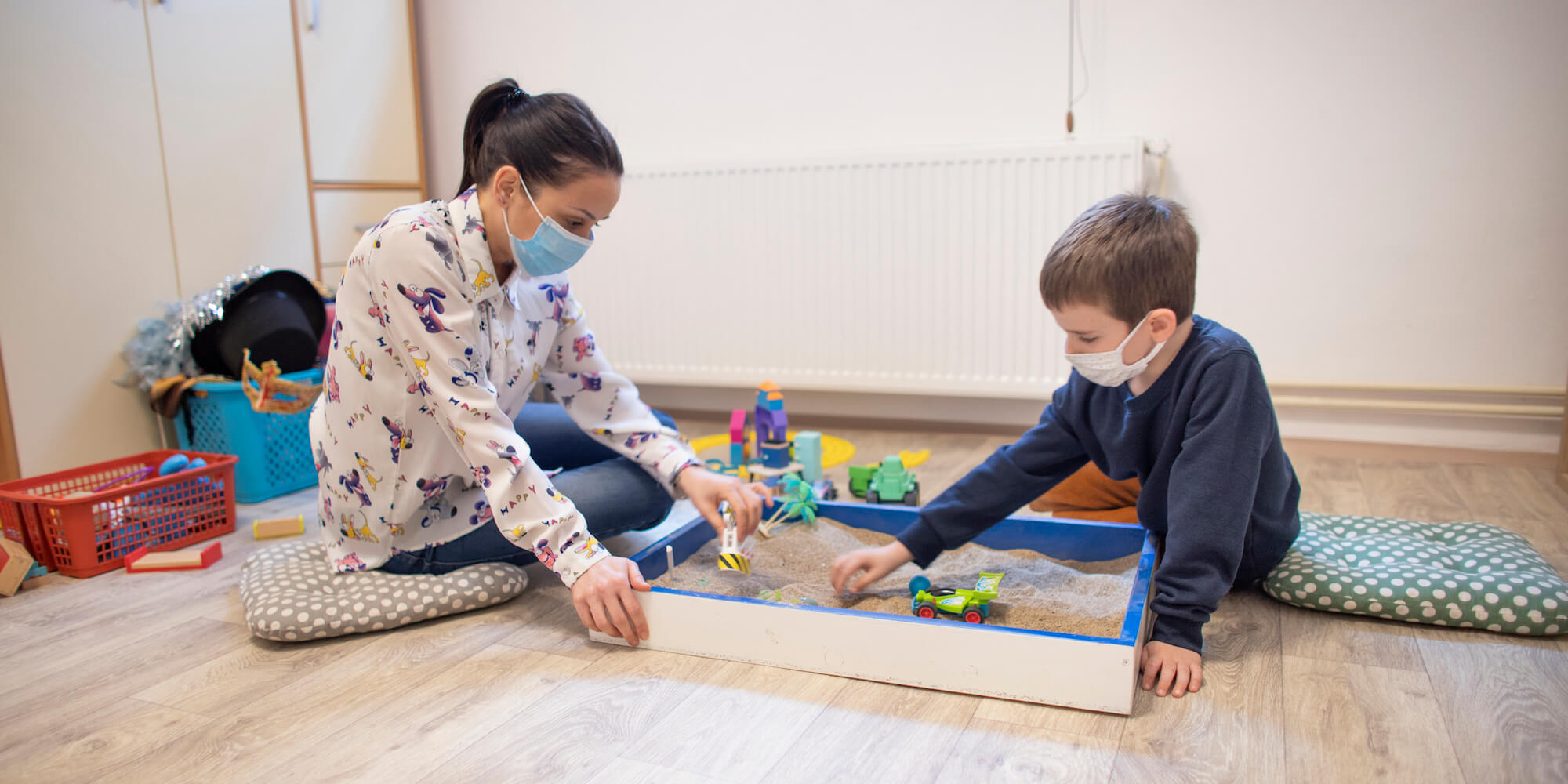 Image showing a young woman and young boy playing with toys in a sand play area. Image from iStock-13104219