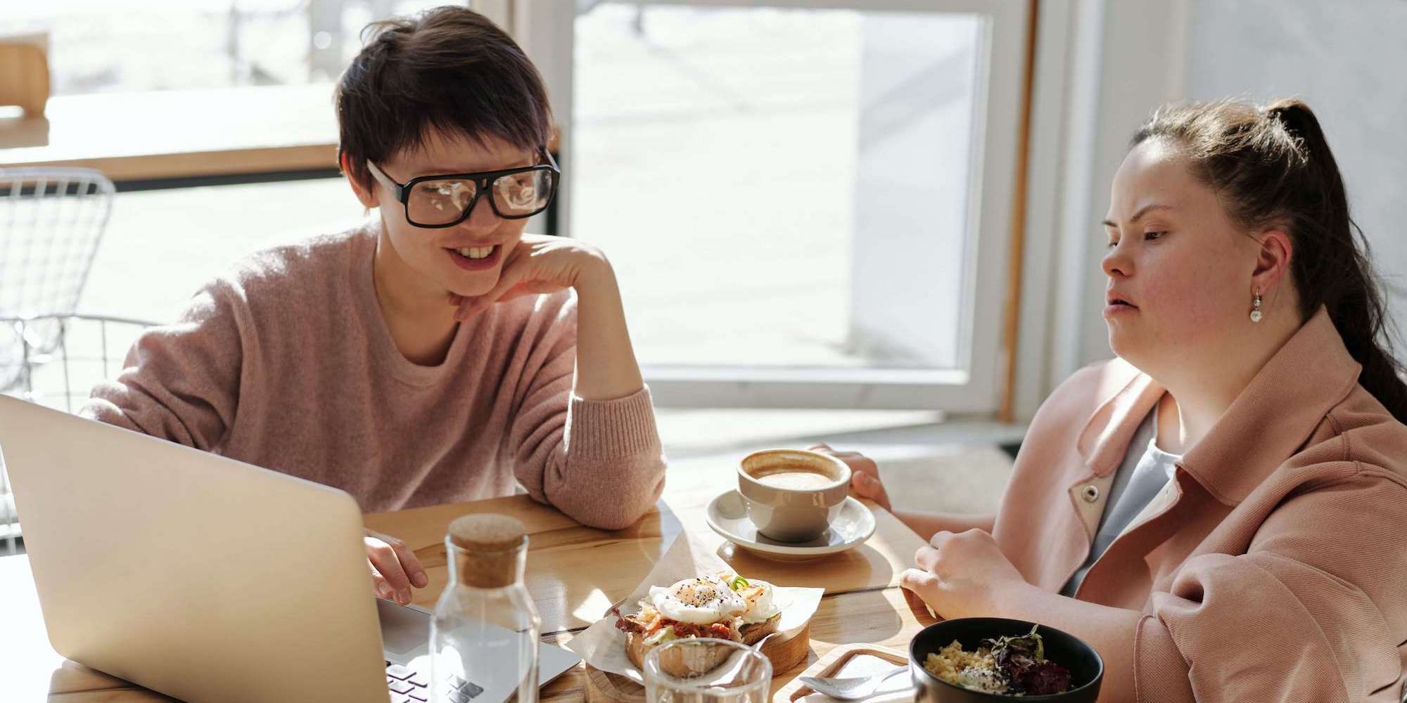 Image showing two ladies sitting at a table with coffee and a laptop. Image from Pexels (Photographer - Cliff Booth)