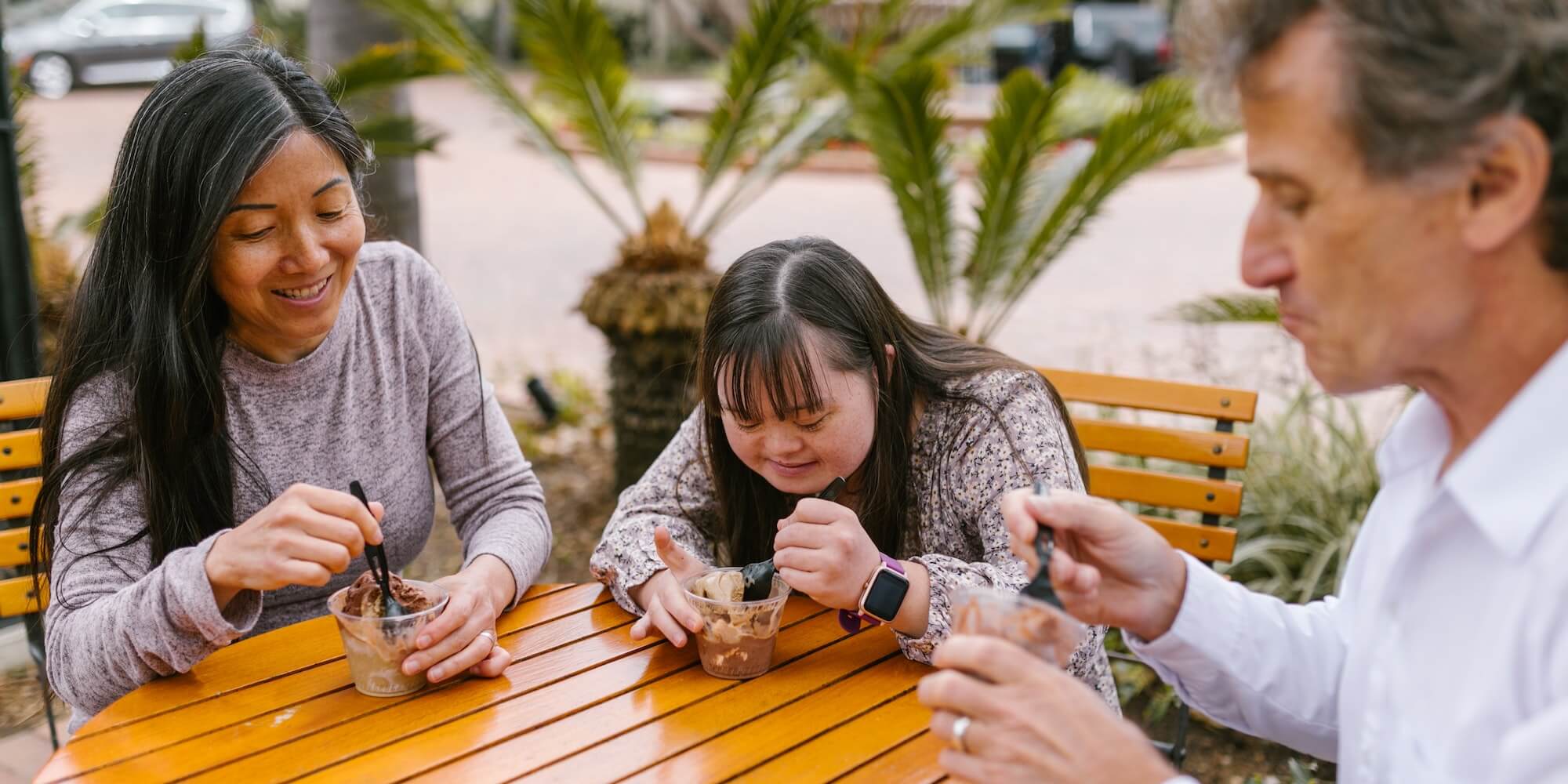 Photo showing a family with a daughter with Downs Syndrome, eating ice cream on an outside table. Photo from Pexels (Photographer Rodnae Productions)