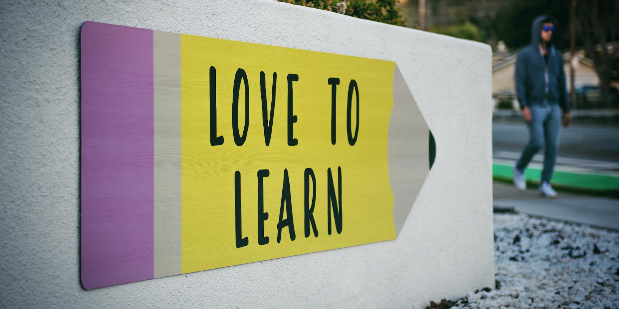 Photo shows a sign shaped like a pencil that says 'Love to Learn'. Image from Unsplash (Photographer is Tim Mossholder)
